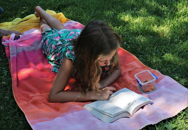 A girl lying on a colourful blanket on the grass, reading a book