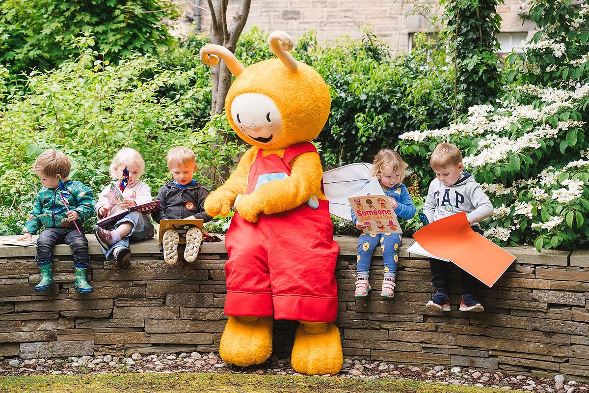 Bookbug surrounded by children sitting on wall reading picture books
