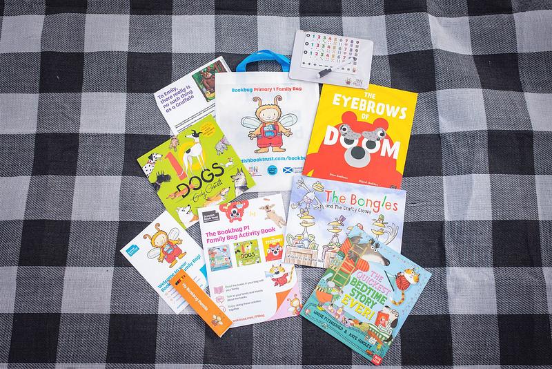 Contents of the 2024 Bookbug P1 Family Bag spread out on a chequered picnic mat