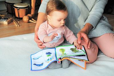 baby looks at colourful cloth picture book of objects with adult