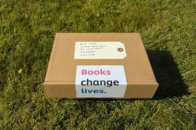 Brown cardboard box package address to 'book lover' with a label saying 'Books Change Lives' lies on grass in sunshine