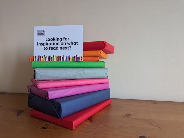 Pile of books wrapped in rainbow coloured tissue paper with a card on top saying 'looking for inspiration on what to read next?'